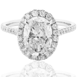 Anello di fidanzamento in oro bianco con diamante ovale centrale e halo di piccoli diamanti lungo il castone e il gambo.
