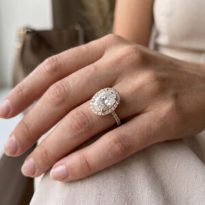 Mano femminile indossa un anello halo in oro rosa con diamante ovale centrale e pavé di piccoli diamanti sulla fascia.